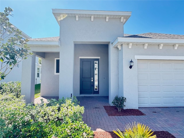 property entrance featuring stucco siding, roof with shingles, and an attached garage