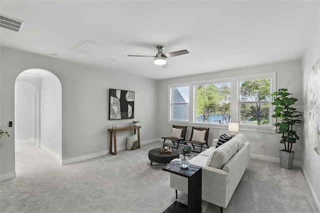 carpeted living room with arched walkways, ceiling fan, visible vents, baseboards, and attic access