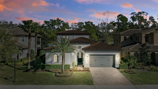 mediterranean / spanish-style home featuring a tile roof, an attached garage, decorative driveway, a front lawn, and stucco siding