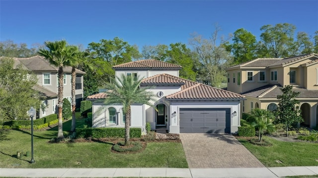 mediterranean / spanish-style home featuring a tile roof, an attached garage, decorative driveway, a front lawn, and stucco siding