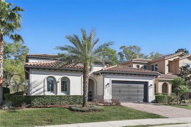 mediterranean / spanish-style house featuring a front yard, driveway, an attached garage, stucco siding, and a tile roof