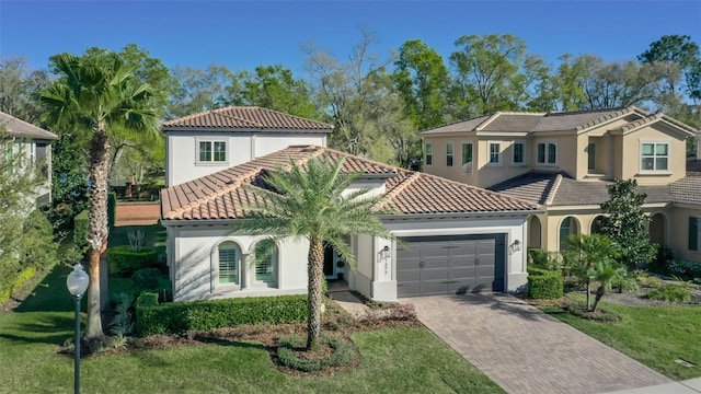 mediterranean / spanish-style home featuring an attached garage, a tile roof, decorative driveway, and stucco siding