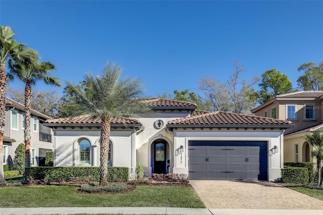 mediterranean / spanish-style home featuring a garage, stucco siding, decorative driveway, and a tiled roof