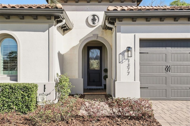 doorway to property with a garage, a tile roof, and stucco siding