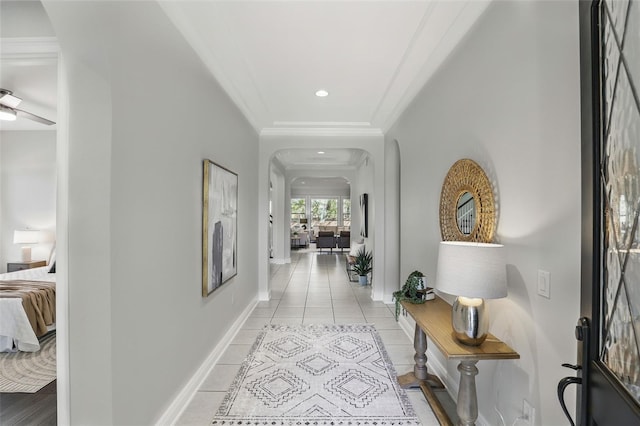 corridor featuring arched walkways, light tile patterned flooring, recessed lighting, baseboards, and crown molding