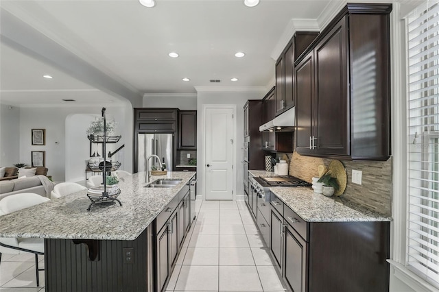 kitchen featuring a breakfast bar, crown molding, a sink, stainless steel fridge, and under cabinet range hood