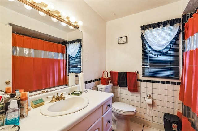 full bathroom featuring toilet, vanity, wainscoting, tile patterned floors, and tile walls