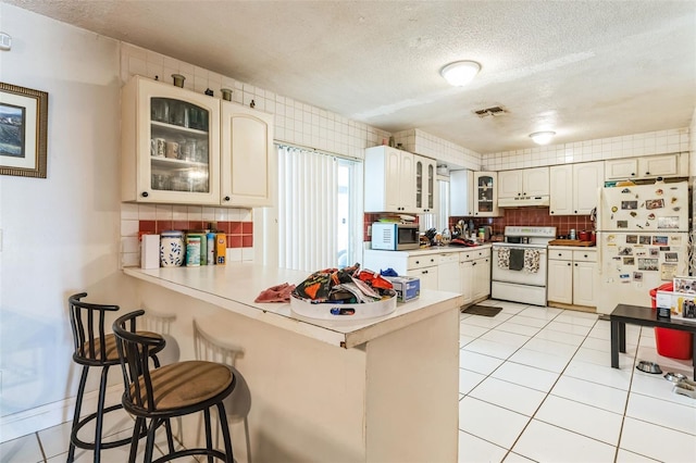 kitchen featuring a breakfast bar, under cabinet range hood, white appliances, a peninsula, and light tile patterned floors