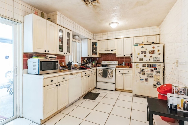 kitchen featuring visible vents, under cabinet range hood, tasteful backsplash, white appliances, and tile walls