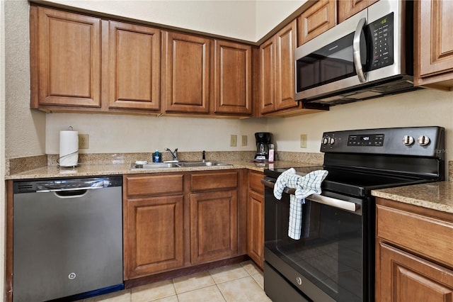 kitchen with light tile patterned floors, appliances with stainless steel finishes, brown cabinetry, and a sink