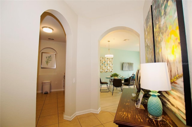 hall featuring arched walkways, visible vents, baseboards, and light tile patterned floors