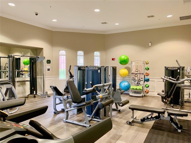 exercise room with wainscoting, visible vents, crown molding, and wood finished floors