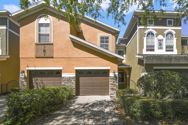 view of front of home featuring stone siding, stucco siding, an attached garage, and decorative driveway