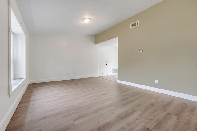 unfurnished room featuring light wood-style floors, visible vents, a textured ceiling, and baseboards