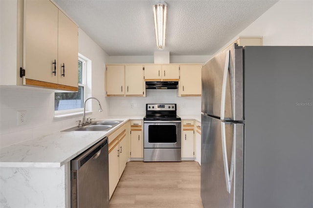 kitchen with stainless steel appliances, tasteful backsplash, cream cabinets, a sink, and exhaust hood