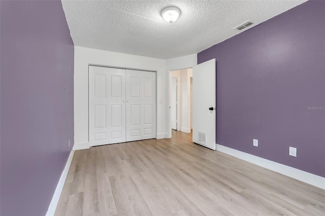 unfurnished bedroom featuring light wood finished floors, baseboards, visible vents, and a closet