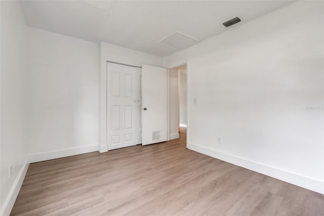 unfurnished bedroom with baseboards, attic access, visible vents, and wood finished floors