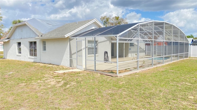 rear view of property featuring a lanai, a shingled roof, a lawn, stucco siding, and a patio area