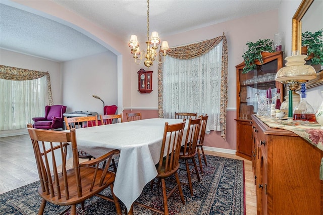 dining room featuring a textured ceiling, arched walkways, light wood finished floors, baseboards, and a chandelier