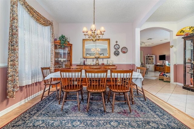 dining area with baseboards, an inviting chandelier, wood finished floors, arched walkways, and a textured ceiling