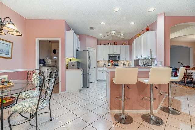 kitchen featuring light tile patterned floors, a peninsula, arched walkways, stainless steel appliances, and white cabinetry