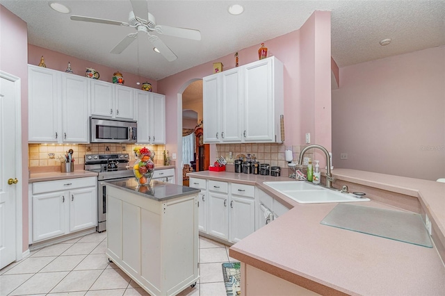 kitchen featuring light tile patterned floors, a peninsula, arched walkways, a sink, and appliances with stainless steel finishes