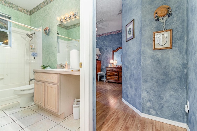 bathroom with toilet, shower / tub combination, wood finished floors, wallpapered walls, and vanity