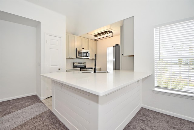 kitchen featuring stainless steel appliances, light countertops, a sink, and a peninsula