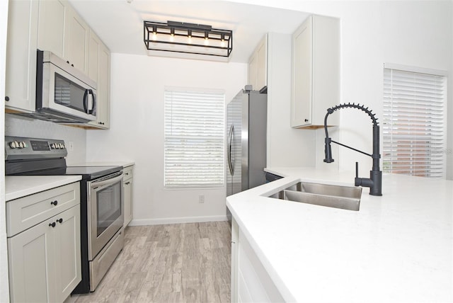 kitchen featuring baseboards, appliances with stainless steel finishes, light countertops, light wood-style floors, and a sink