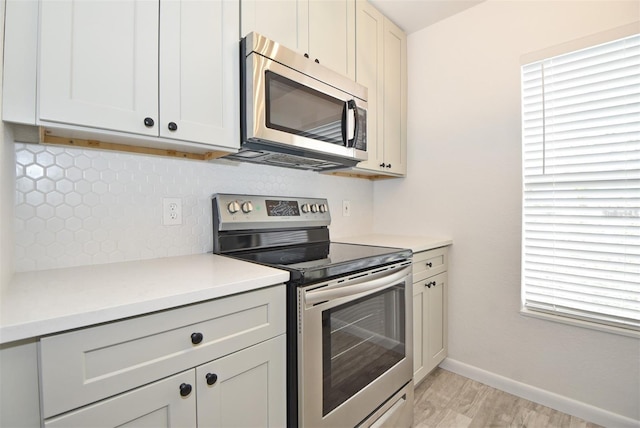 kitchen with stainless steel appliances, baseboards, light countertops, light wood finished floors, and tasteful backsplash