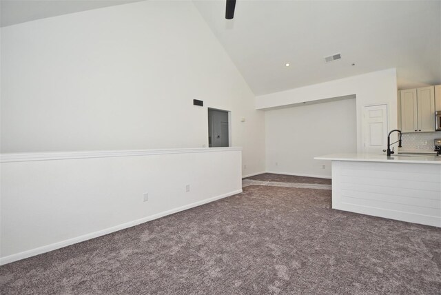 unfurnished living room with baseboards, visible vents, dark carpet, high vaulted ceiling, and a sink