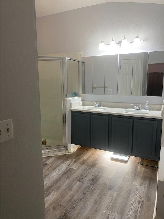 full bath featuring double vanity, a stall shower, wood finished floors, and a sink