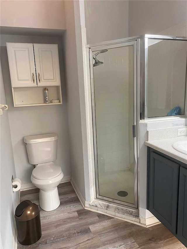 bathroom with a shower stall, baseboards, toilet, wood finished floors, and vanity