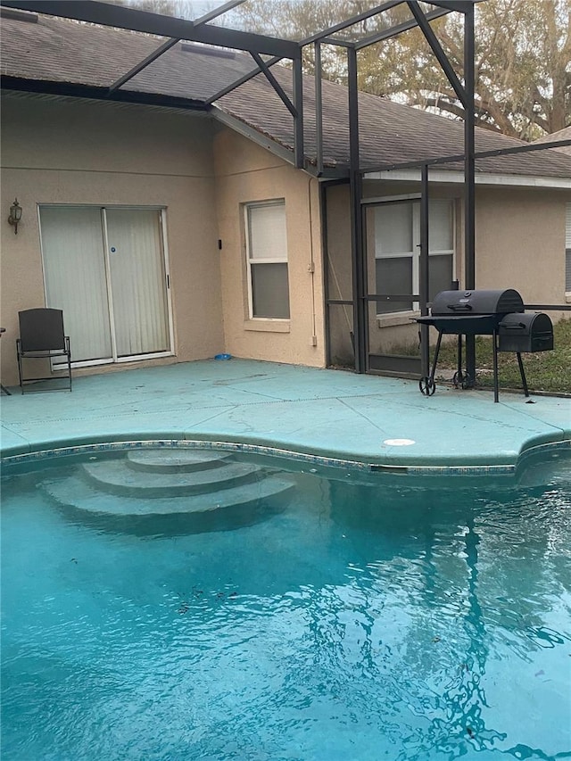 pool with glass enclosure, a grill, and a patio