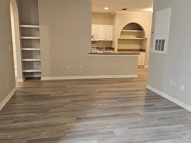 unfurnished living room featuring built in features, baseboards, wood finished floors, and ornamental molding