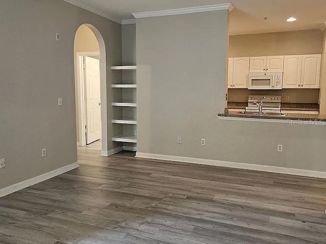 unfurnished living room featuring arched walkways, dark wood-type flooring, a sink, baseboards, and ornamental molding