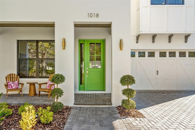 view of exterior entry featuring stucco siding, decorative driveway, and a garage