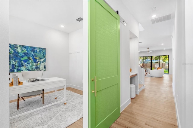 office space featuring visible vents, baseboards, light wood-type flooring, and a barn door