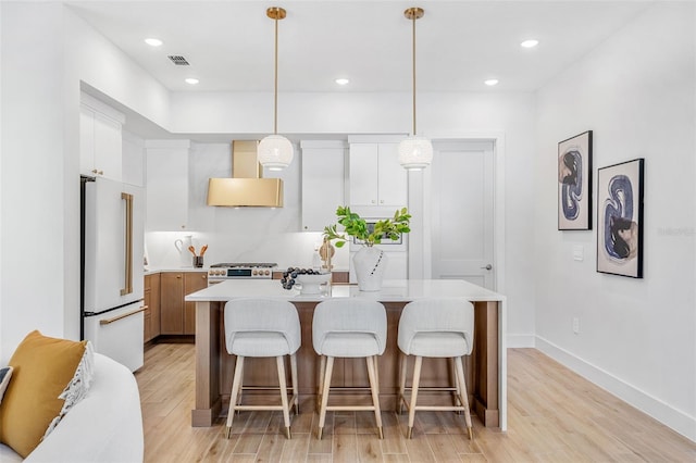 kitchen with gas stove, freestanding refrigerator, light countertops, wall chimney range hood, and a center island