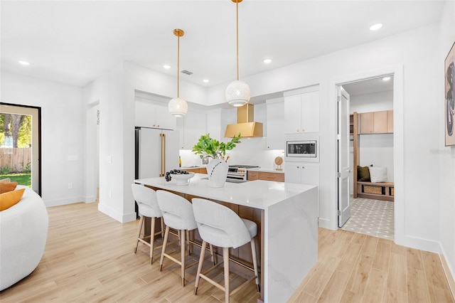 kitchen with light wood-style flooring, wall chimney range hood, a kitchen breakfast bar, appliances with stainless steel finishes, and light countertops