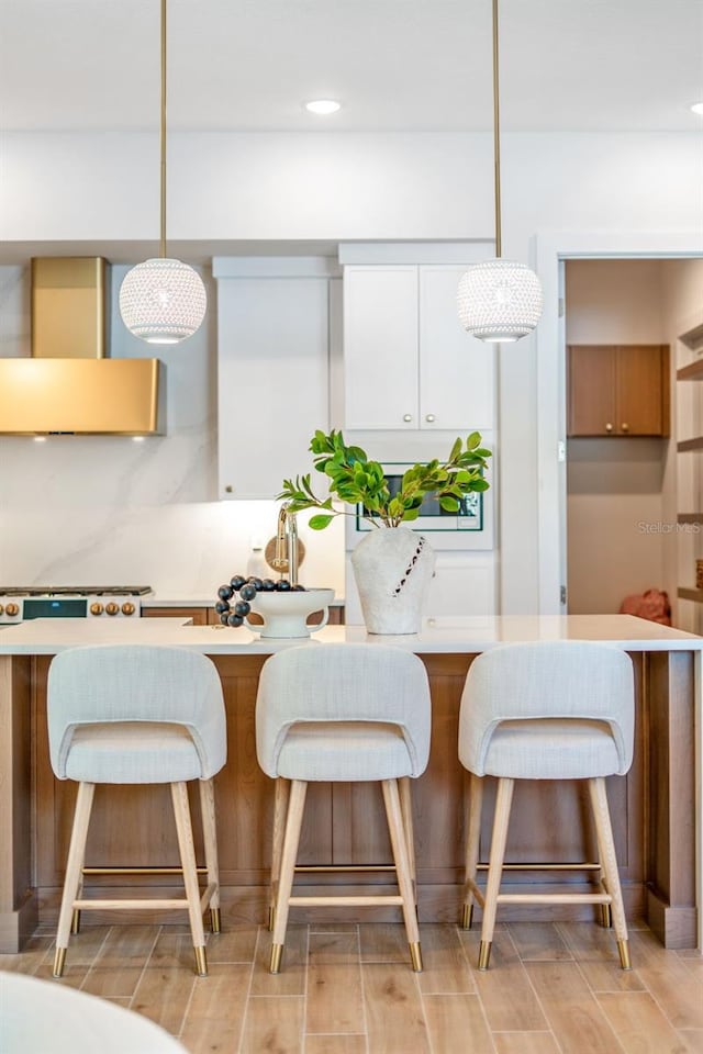 kitchen with decorative light fixtures, light countertops, wall chimney exhaust hood, and wood finish floors