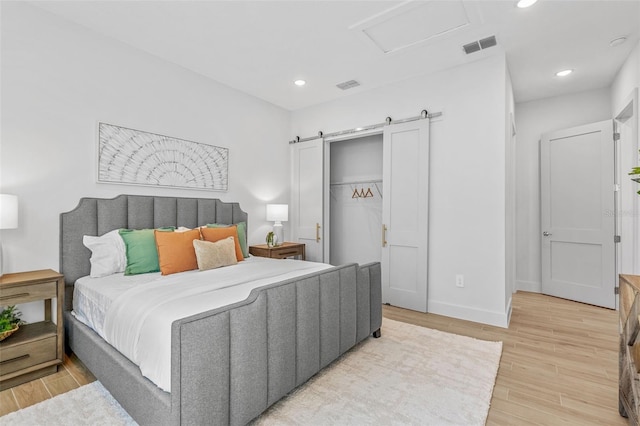 bedroom featuring a barn door, attic access, visible vents, and light wood finished floors