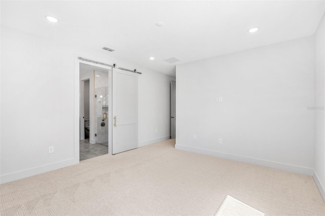 unfurnished bedroom featuring recessed lighting, visible vents, light colored carpet, and a barn door