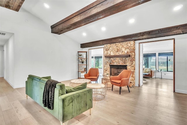 living area with light wood-type flooring, baseboards, a stone fireplace, and vaulted ceiling with beams