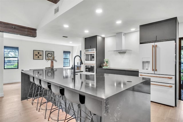 kitchen featuring visible vents, a spacious island, white refrigerator with ice dispenser, light wood-style floors, and wall chimney exhaust hood