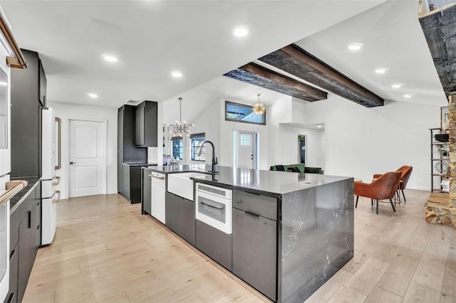 kitchen with white appliances, an inviting chandelier, light wood-style flooring, a sink, and dark countertops