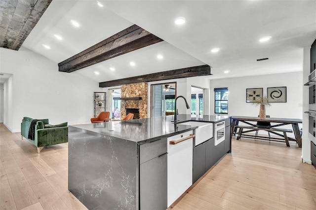 kitchen with light wood-type flooring, a sink, open floor plan, a stone fireplace, and a large island with sink