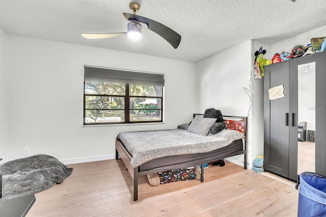 bedroom with ceiling fan, baseboards, a textured ceiling, and wood finished floors