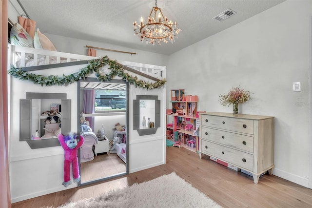 bedroom with baseboards, visible vents, an inviting chandelier, light wood-style flooring, and a textured ceiling