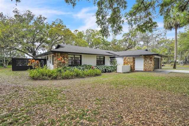 view of front of home featuring a front yard, an attached garage, stone siding, and driveway